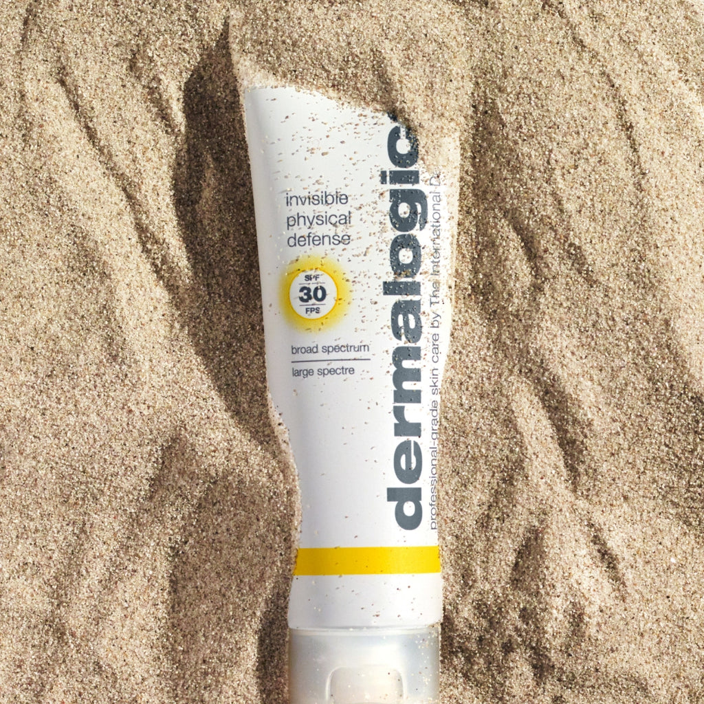 ダーマロジカ インビジブル フィジカル ディフェンス SPF30 — 砂浜に置かれた日焼け止めチューブの夏のビーチライフスタイルイメージ | 日焼け止め