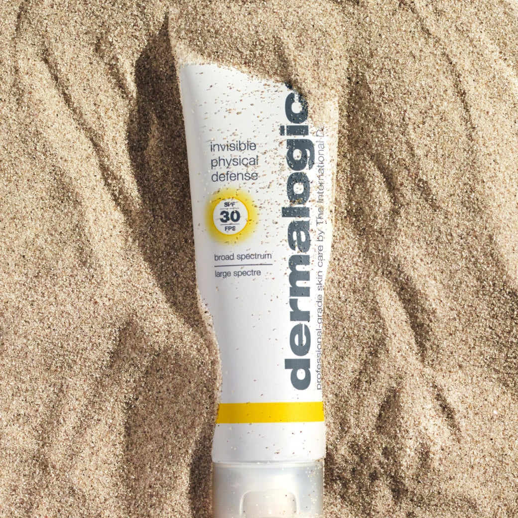 ダーマロジカ インビジブル フィジカル ディフェンス SPF30 — 砂浜に置かれた日焼け止めチューブの夏のビーチライフスタイルイメージ | 日焼け止め